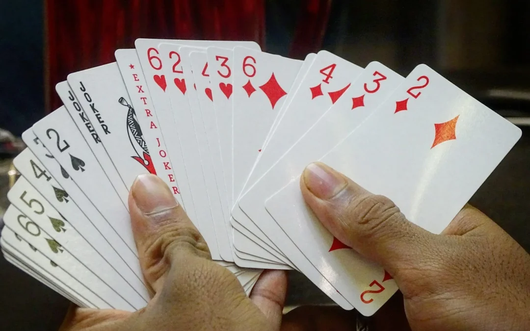A hand holding playing cards fanned out, showing a joker and number cards.
