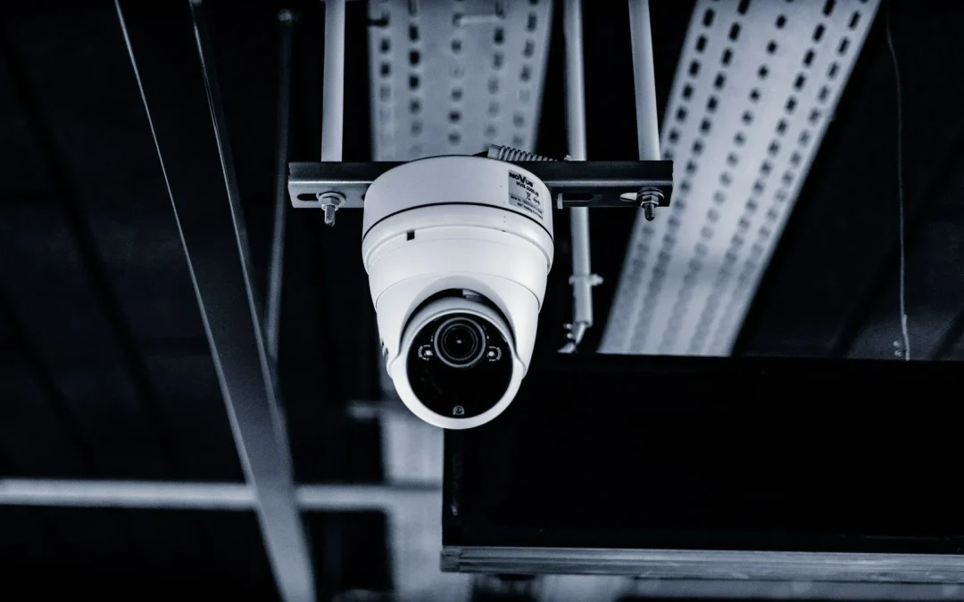 Security camera mounted on a ceiling, focusing downwards, with industrial elements in the background.